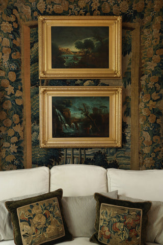 Pair of antique French landscape paintings with moody blue and green tones in front of tapestry