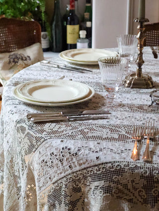 Antique French filet lace tablecloth laid on dining table with silver candlesticks and crystal glasses