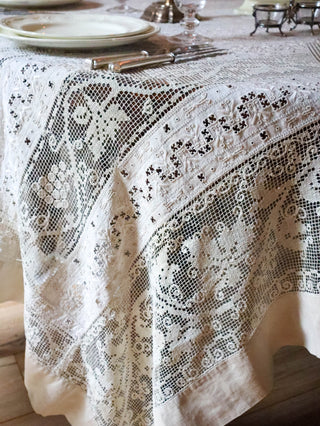 Close-up of antique filet lace tablecloth showing hand-worked grape vine and linen border detail
