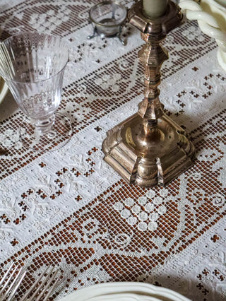 Detail of antique French filet lace tablecloth with silver candlestick and crystal wine glass