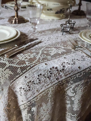Antique lace tablecloth styled for dinner party with lit candle, vintage soup tureen and pressed botanicals in background