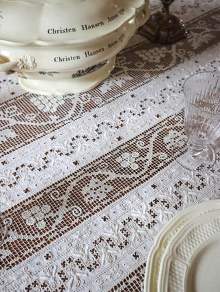 Detail of antique French filet lace tablecloth with silver candlestick and crystal wine glass
