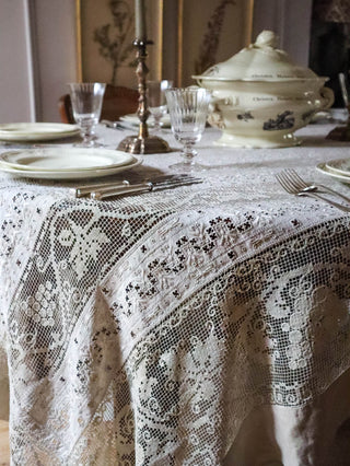 Antique lace tablecloth styled for dinner party with lit candle, vintage soup tureen and pressed botanicals in background