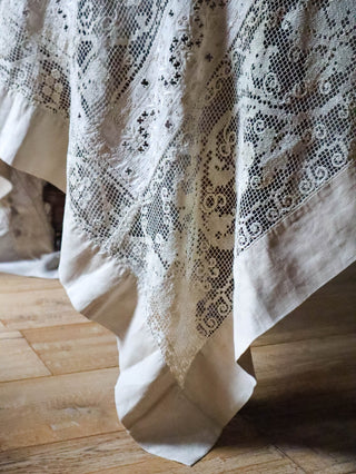 Close-up of antique filet lace tablecloth showing hand-worked grape vine and linen border detail