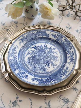 Set of seven blue and white chinoiserie transferware plates with scalloped edge, styled with a silver charger and white roses